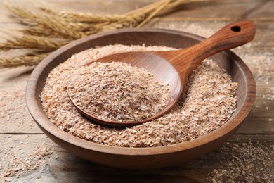 Photo of Wheat bran and spoon in bowl on wooden table