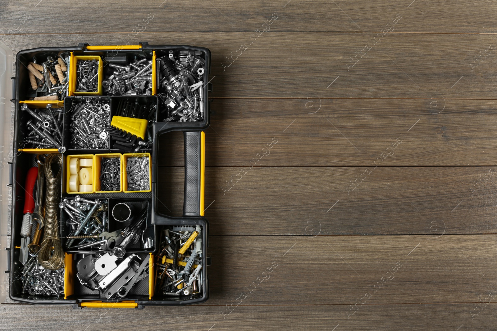 Photo of Box with different furniture fittings and tools on wooden table, top view. Space for text