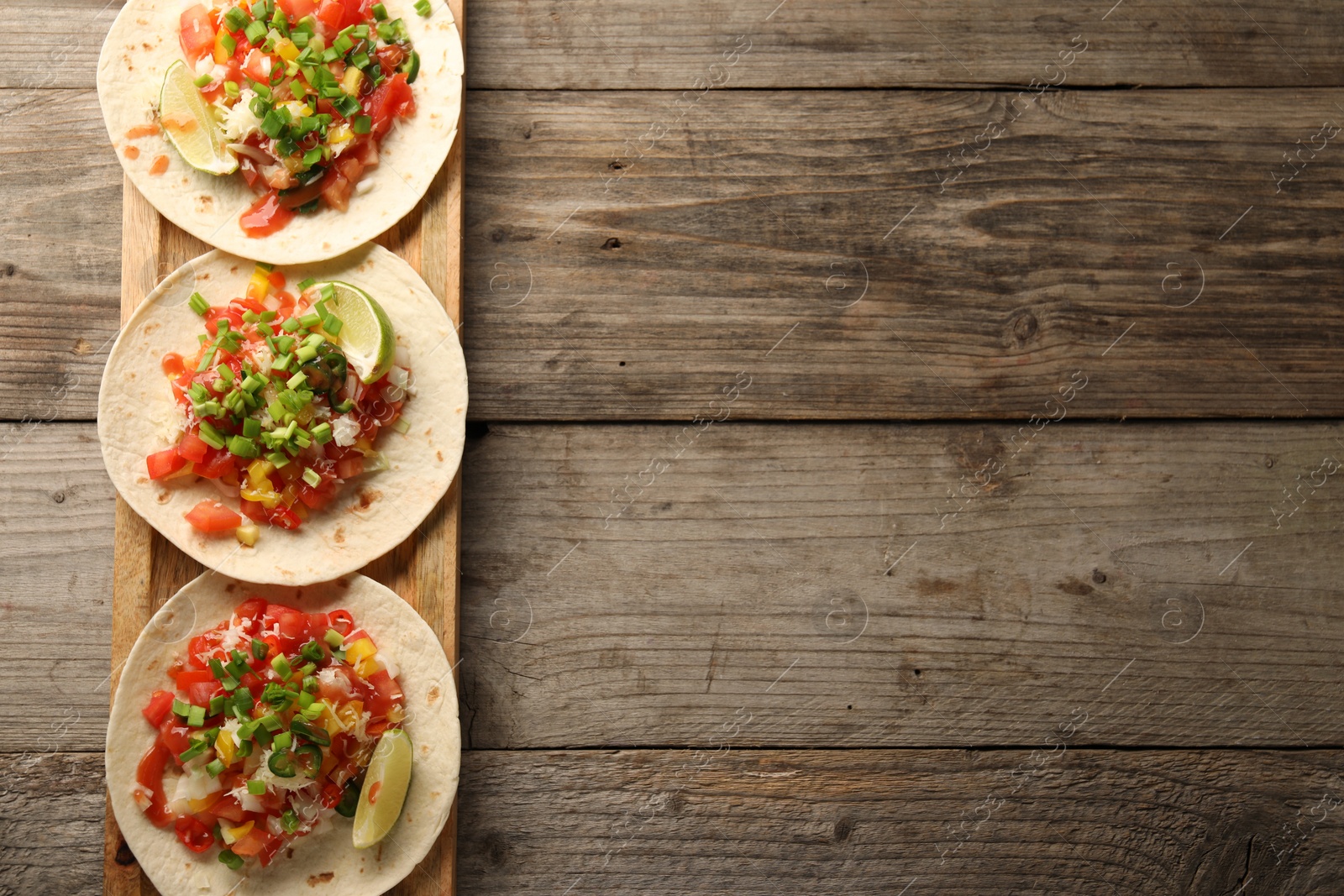 Photo of Delicious tacos with vegetables, green onion, lime and ketchup on wooden table, top view. Space for text