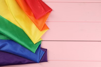 Photo of Rainbow LGBT flag on pink wooden table, top view. Space for text