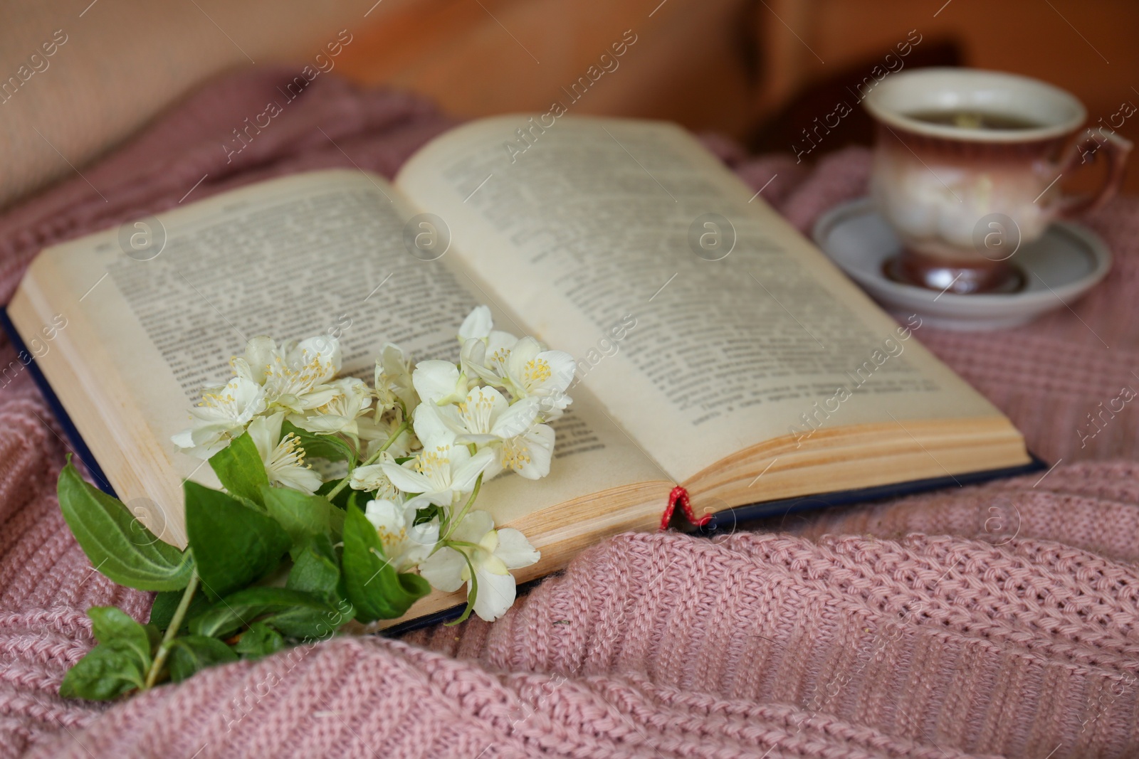 Photo of Beautiful jasmine flowers, open book and cup of aromatic drink on pink fabric