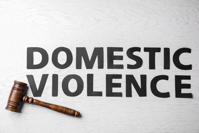 Photo of Words DOMESTIC VIOLENCE and gavel on white wooden table, flat lay