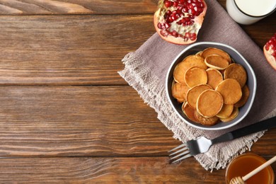 Photo of Delicious mini pancakes cereal served on wooden table, flat lay. Space for text
