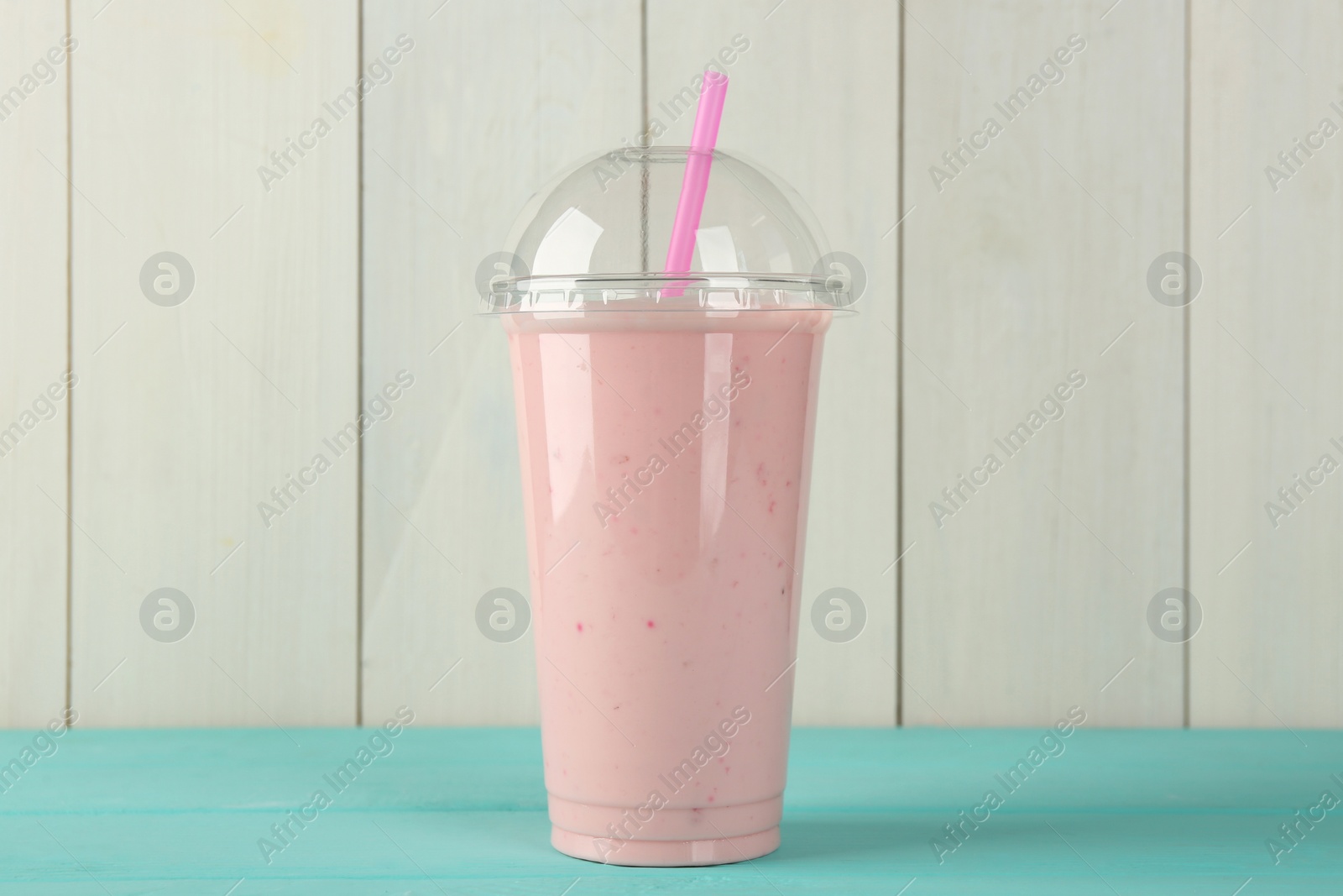 Photo of Tasty smoothie in plastic cup on light blue table against white wooden wall