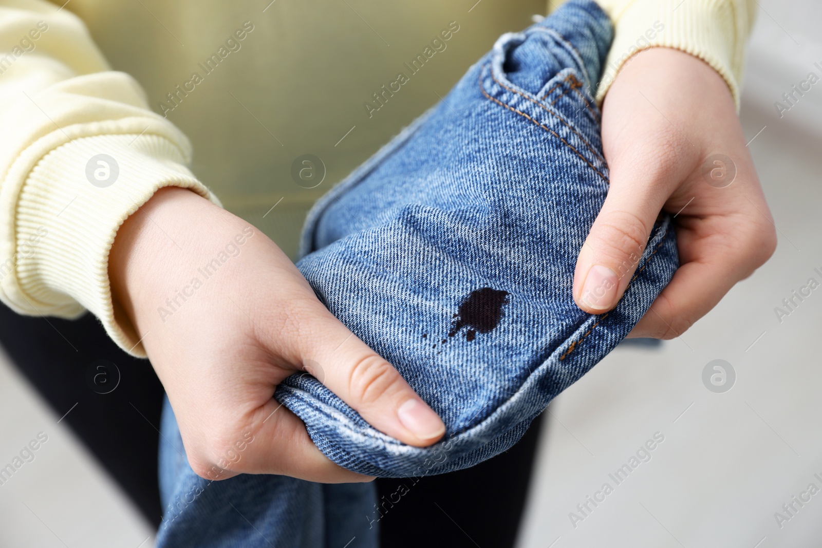 Photo of Woman holding jeans with black ink stain on blurred background, closeup