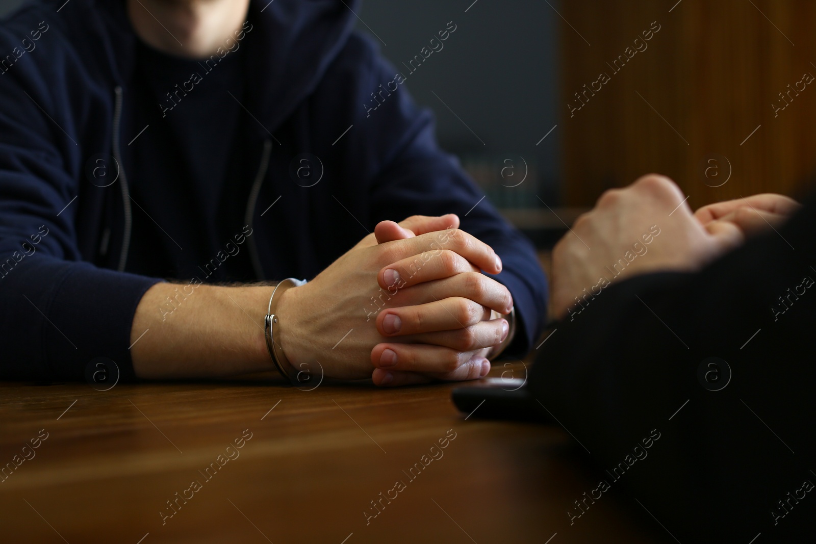 Photo of Police officer interrogating criminal in handcuffs at desk indoors