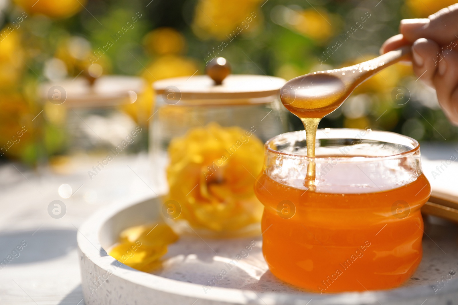 Photo of Woman pouring honey into glass jar at white wooden table, closeup. Space for text