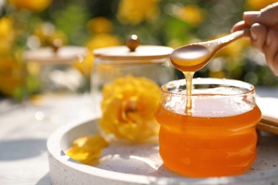 Woman pouring honey into glass jar at white wooden table, closeup. Space for text