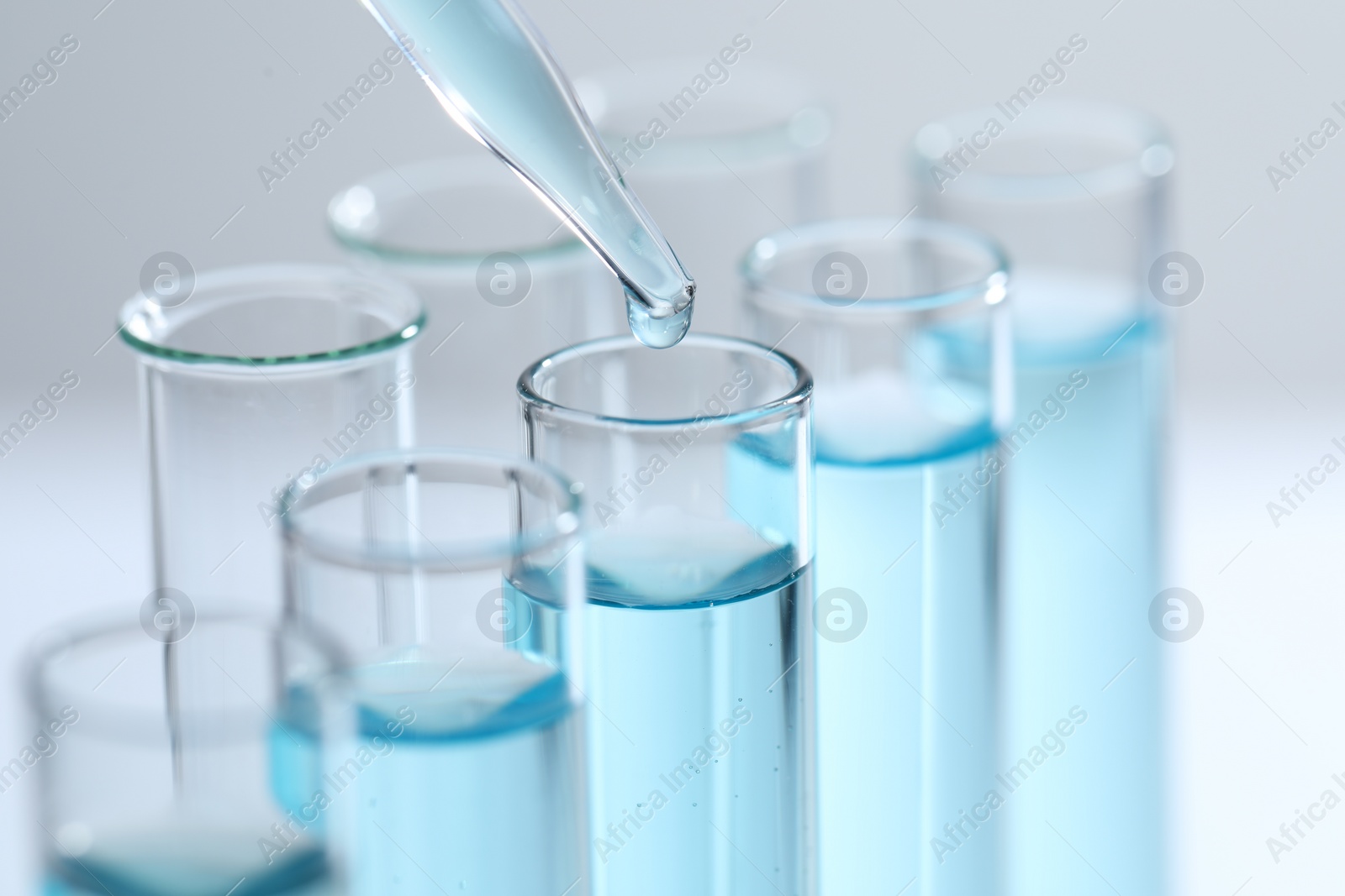 Photo of Dripping liquid from pipette into test tube on light background, closeup