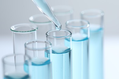 Photo of Dripping liquid from pipette into test tube on light background, closeup