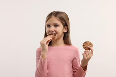 Photo of Cute girl eating chocolate chip cookies on white background