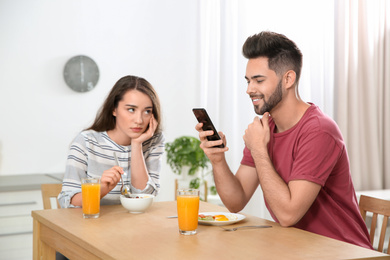 Young man preferring smartphone over his girlfriend at home