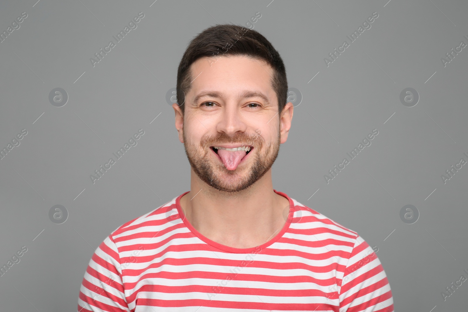 Photo of Happy man showing his tongue on grey background