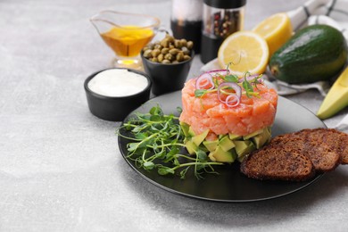 Photo of Tasty salmon tartare with avocado, microgreens and croutons on grey table, space for text