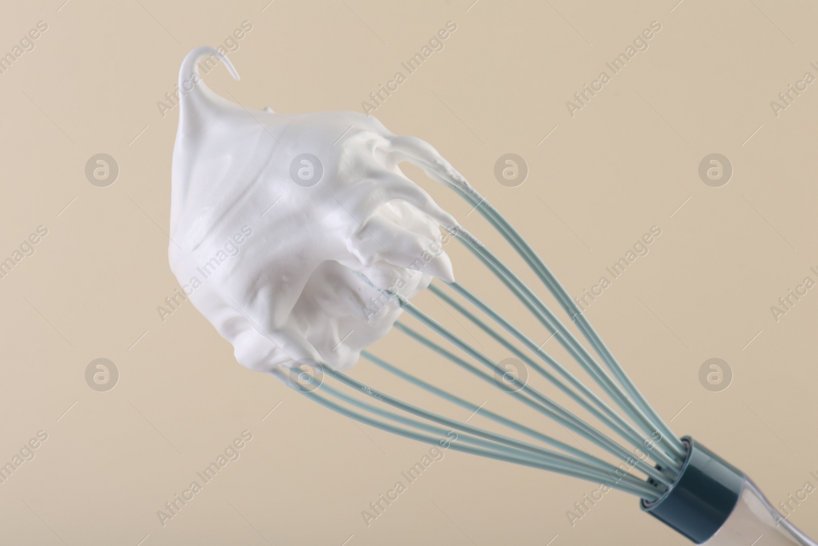 Photo of Whisk with whipped cream on beige background, closeup