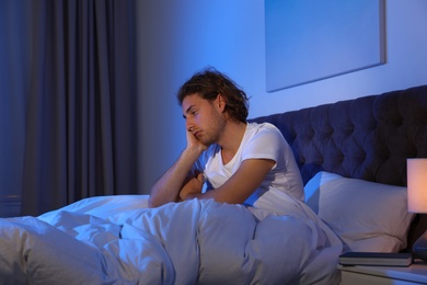 Photo of Handsome young man suffering from insomnia in dark room at night. Bedtime