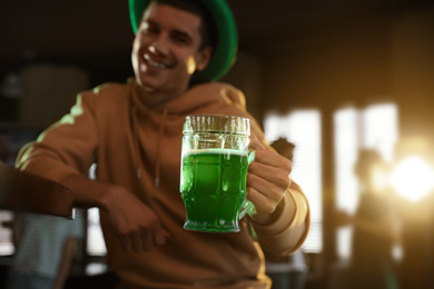 Photo of Man holding glass of green beer in pub, focus on hand. St. Patrick's Day celebration