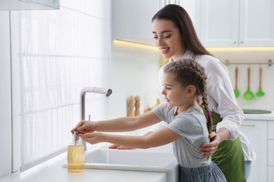 Mother and daughter washing hands with liquid soap in kitchen