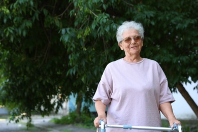 Photo of Elderly woman using walking frame in park. Space for text