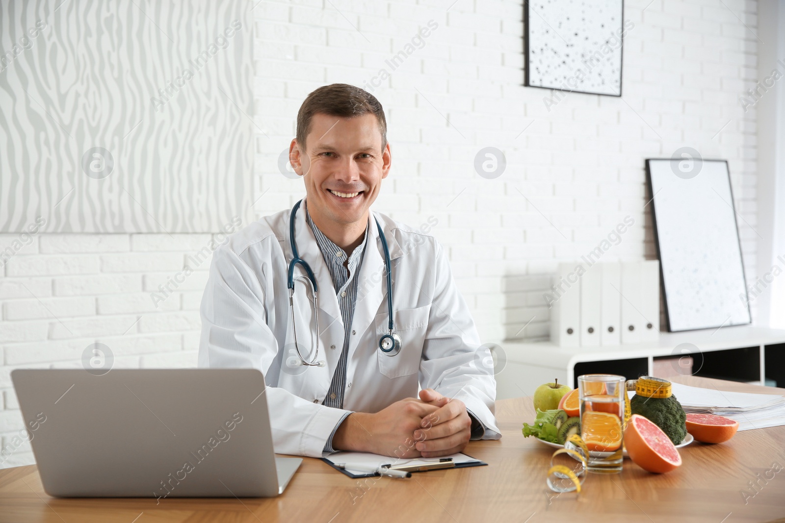 Photo of Nutritionist with clipboard and laptop at desk in office