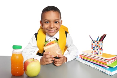 African-American schoolboy with healthy food and backpack sitting at table on white background