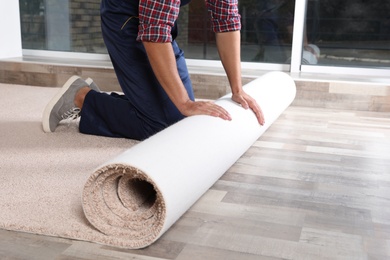 Photo of Man rolling out new carpet flooring indoors, closeup