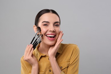Happy woman with different makeup brushes on light grey background