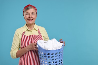 Photo of Happy housewife with basket full of laundry on light blue background, space for text
