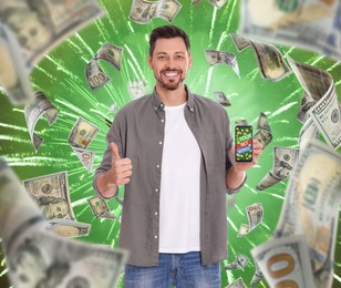 Image of Your Bet Wins! Happy man holding smartphone and showing thumb up under money shower against green background with firework