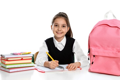 Photo of Little girl in uniform doing assignment at desk against white background. School stationery