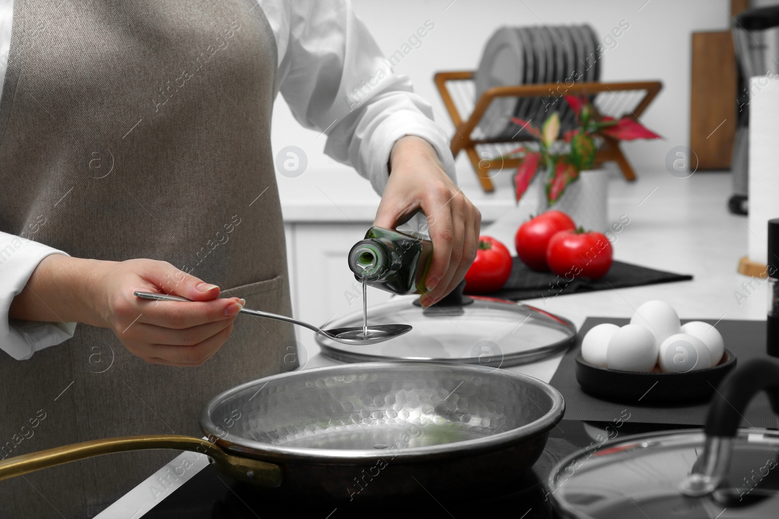 Photo of Woman pouring cooking oil from bottle into frying pan in kitchen, closeup