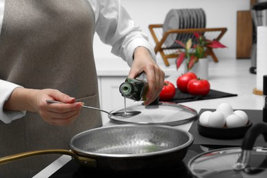 Woman pouring cooking oil from bottle into frying pan in kitchen, closeup