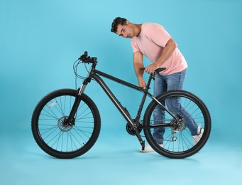 Handsome young man with modern bicycle on light blue background