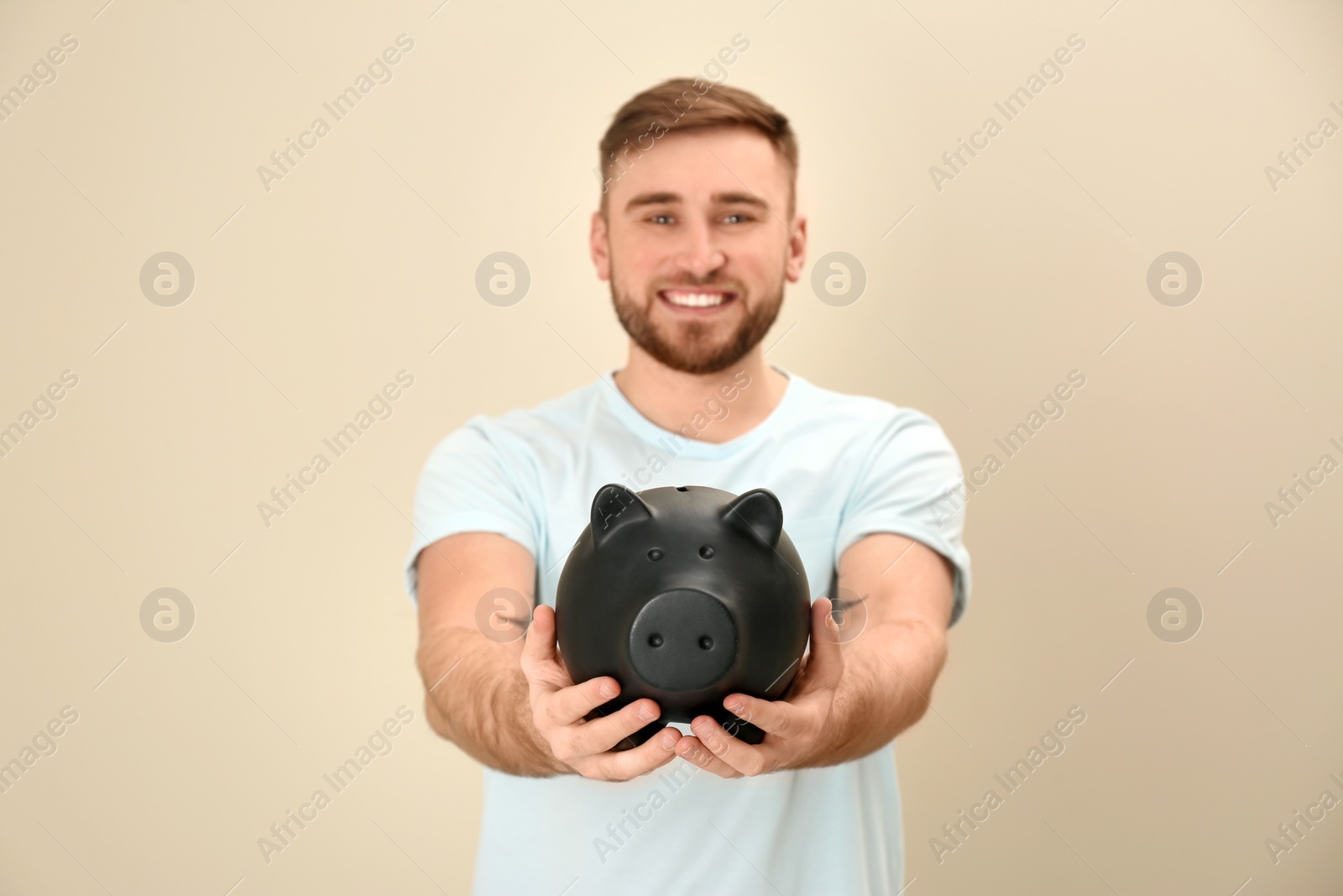 Photo of Portrait of happy young man with piggy bank on color background. Money saving