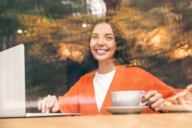 Photo of Special Promotion. Happy young woman with cup of drink using laptop in cafe, view from outdoors