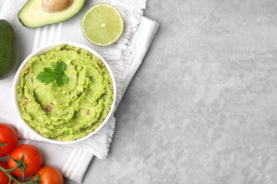 Photo of Bowl of delicious guacamole and ingredients on grey table, flat lay. Space for text