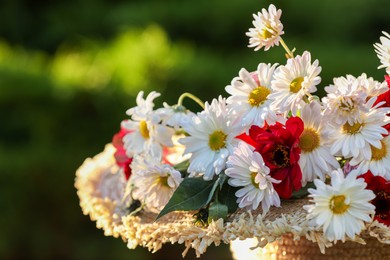 Photo of Beautiful wild flowers in wicker basket against blurred background, closeup. Space for text