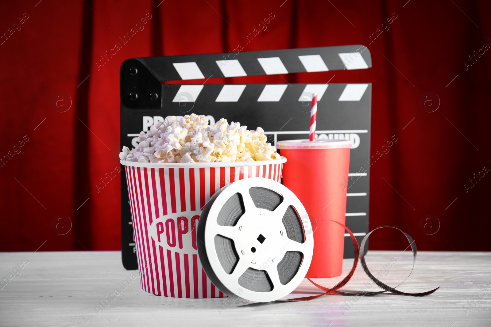 Photo of Clapperboard, reel and popcorn bucket on table against stage curtain. Watching cinema