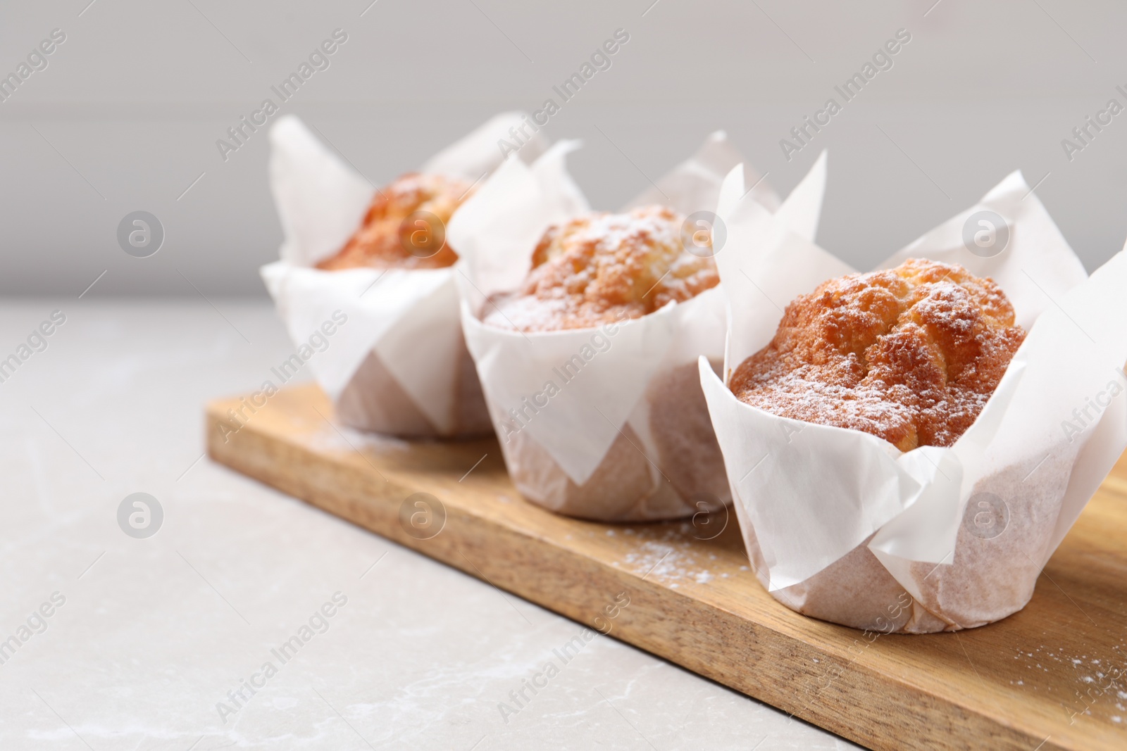 Photo of Delicious muffins with powdered sugar on light table, closeup