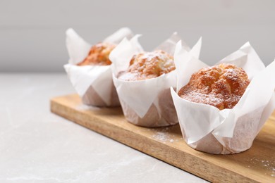 Photo of Delicious muffins with powdered sugar on light table, closeup