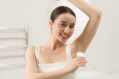 Beautiful young woman applying deodorant in bathroom