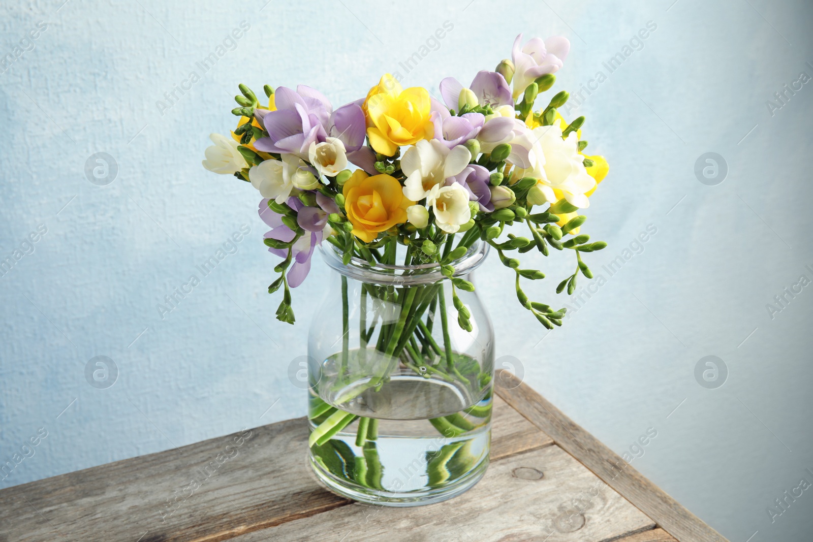 Photo of Bouquet of fresh freesia flowers in glass vase on table