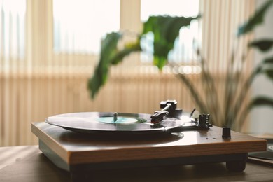 Photo of Stylish turntable with vinyl disc on wooden table indoors, space for text