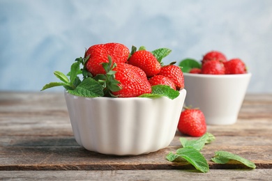 Photo of Bowl with ripe red strawberries and mint on wooden table