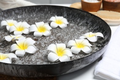 Bowl of water with plumeria flowers on table, closeup