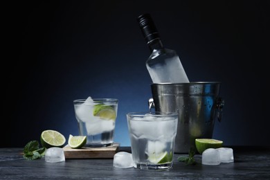 Bottle of vodka, glasses, lime, mint and ice on black marble table
