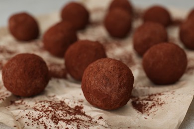 Photo of Delicious chocolate candies powdered with cocoa on parchment paper, closeup