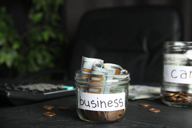 Photo of Glass jar with money and tag BUSINESS on black table