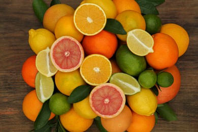 Different citrus fruits with green leaves on wooden table, flat lay