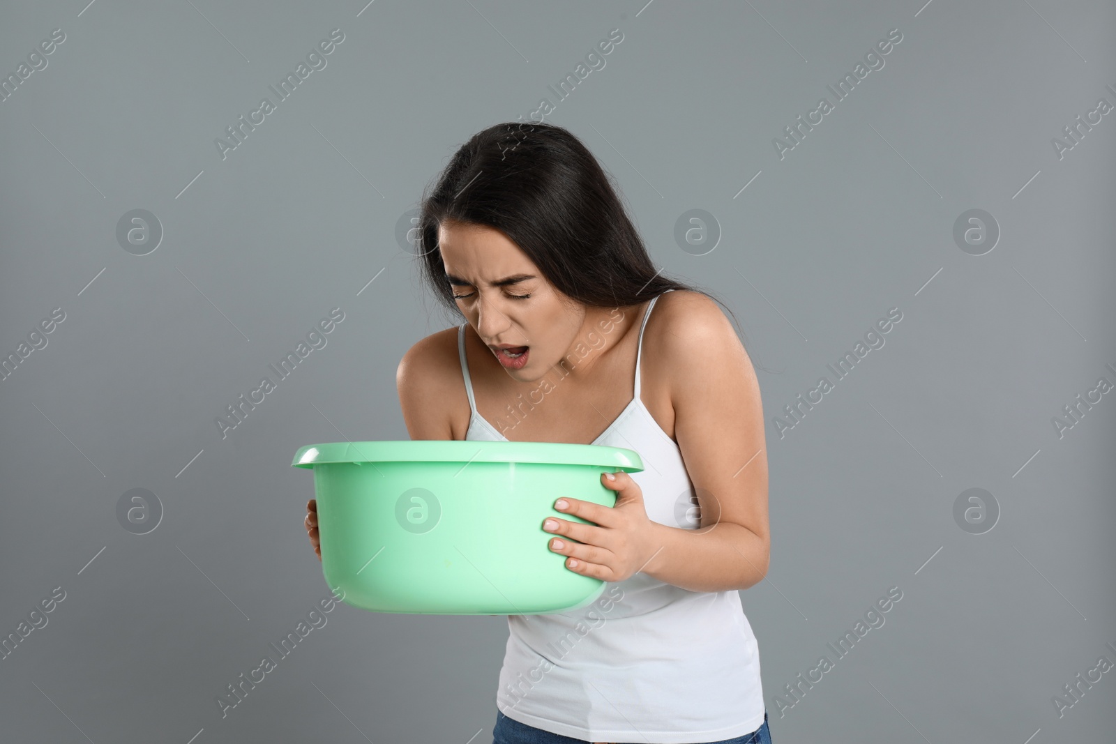 Photo of Young woman with basin suffering from nausea on grey background. Food poisoning